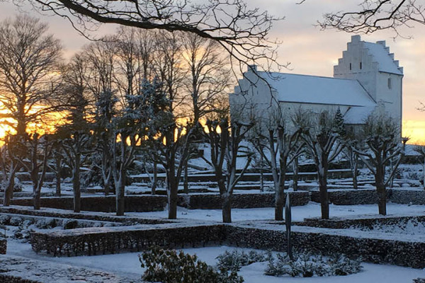 Hvalsø Kirke og kirkegård med sne og sol i baggrund